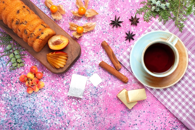 Vista dall'alto deliziosa torta dolce e gustosa con prugne tazza di tè e ciliegie dolci sulla scrivania rosa.