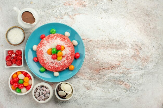 Vista dall'alto deliziosa torta rosa con caramelle colorate e biscotti su superficie bianca biscotto caramelle color arcobaleno