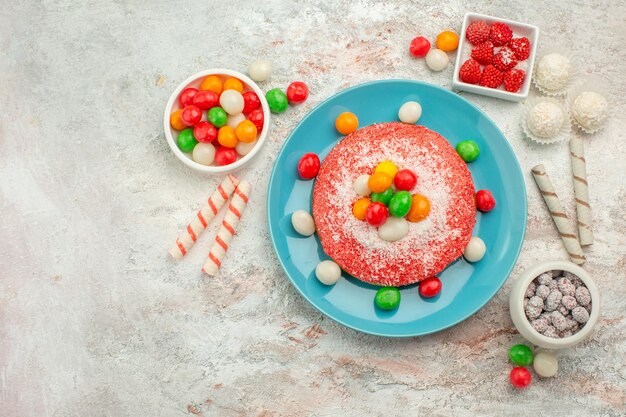 Vista dall'alto deliziosa torta rosa con caramelle colorate su scrivania bianca caramelle dessert color arcobaleno goodie cake