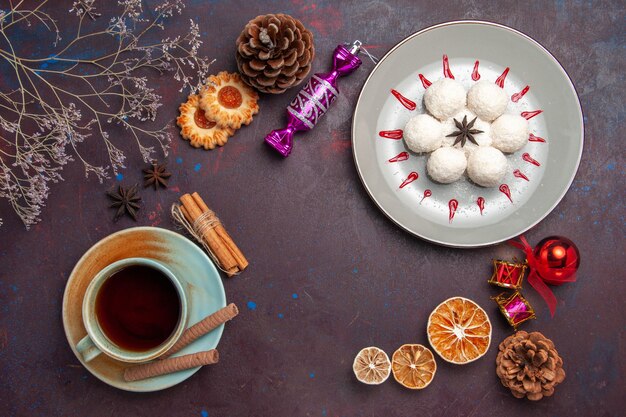 Vista dall'alto deliziose caramelle al cocco piccole e rotonde formate con una tazza di tè su sfondo scuro caramelle al cocco torta dolce biscotto tè