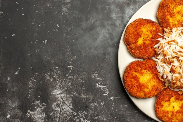 Vista dall'alto deliziose cotolette fritte con riso cotto su un piatto di carne di superficie scura