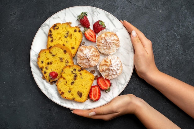 Vista dall'alto deliziose fette di torta con fragole rosse fresche e biscotti sulla superficie grigia