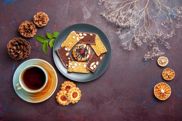 Vista dall'alto deliziose fette di torta con un po' di biscotto e tazza di tè sulla scrivania scura biscotto biscotto dessert torta tè dolce