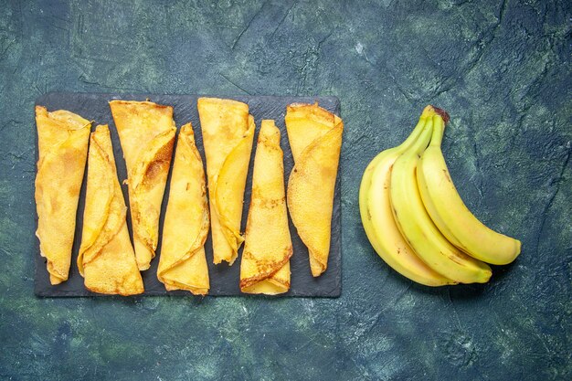 Vista dall'alto deliziose frittelle arrotolate con banane su sfondo scuro pasta per torta hotcake farina colorata pasticceria carne di torta