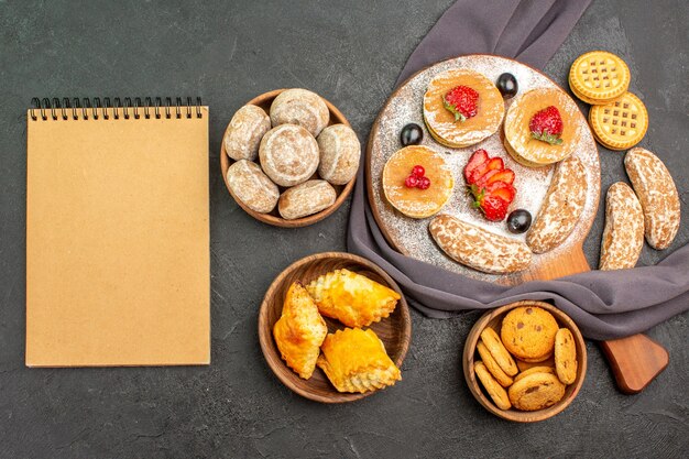 Vista dall'alto deliziose frittelle con frutta e torte dolci sul pavimento scuro