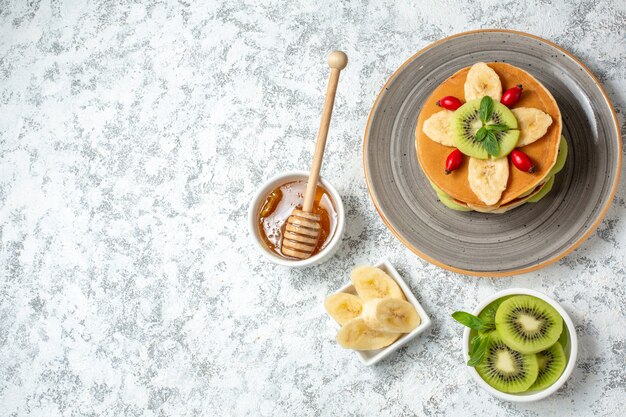 Vista dall'alto deliziose frittelle con miele e frutta a fette su sfondo bianco frutta dolce dessert colazione colore torta zucchero