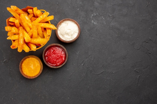 Vista dall'alto deliziose patatine fritte con condimenti su sfondo scuro hamburger fast-food piatto di patate