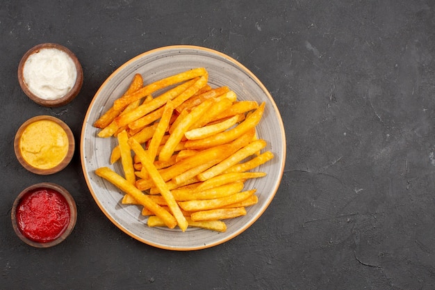 Vista dall'alto deliziose patatine fritte con condimenti sul piatto di fast-food di hamburger di pasto di patate sfondo scuro