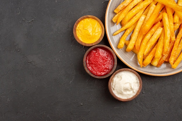 Vista dall'alto deliziose patatine fritte con condimenti sullo sfondo scuro piatto di patate hamburger fast-food