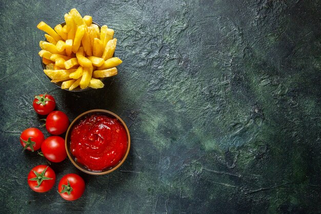 Vista dall'alto deliziose patatine fritte con pomodorini sulla superficie scura