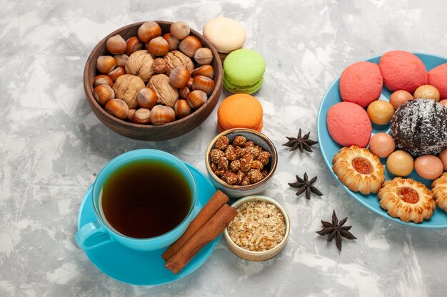 Vista dall'alto deliziose torte con macarons noci tè e biscotti sulla superficie bianca