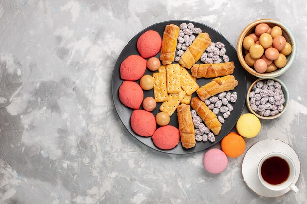 Vista dall'alto deliziose torte con tazza di cracker e caramelle di ciambelle di tè sulla torta di zucchero dolce del biscotto della torta della scrivania bianca chiara