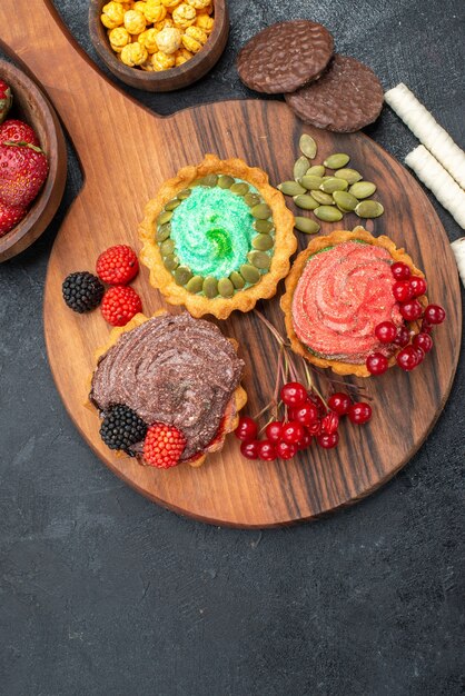 Vista dall'alto deliziose torte cremose con frutta sui biscotti di biscotto dolce tavolo scuro