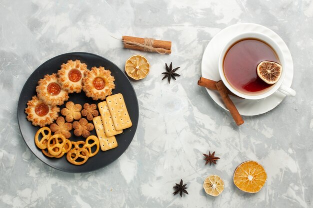 Vista dall'alto deliziosi biscotti con cracker e patatine all'interno del piatto con una tazza di tè sulla scrivania bianca biscotto biscotto zucchero tè dolce croccante