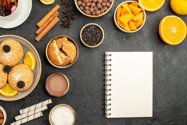 Vista dall'alto deliziosi biscotti con fette d'arancia e tazza di tè sulla superficie scura torta torta zucchero dessert biscotto tè