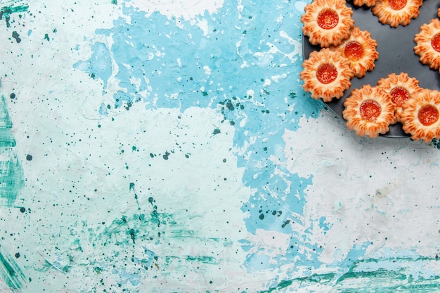 Vista dall'alto deliziosi biscotti con marmellata all'interno della banda nera sulla scrivania blu chiaro biscotto biscotto dolce zucchero colore tè