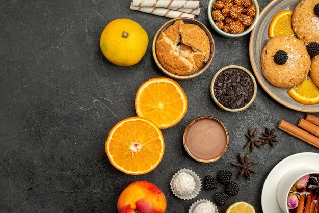 Vista dall'alto deliziosi biscotti con una tazza di tè e fette d'arancia su una torta di biscotti con biscotto al tè con superficie scura