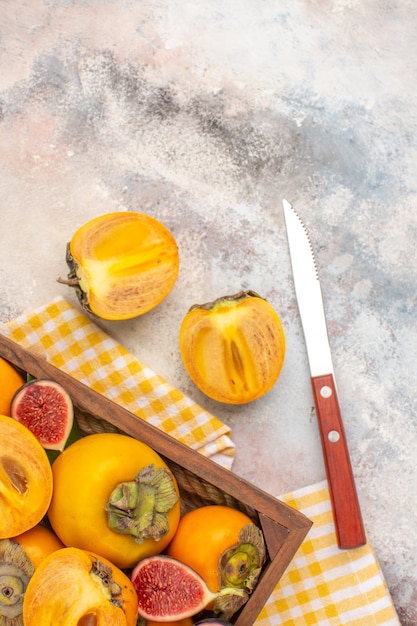 Vista dall'alto deliziosi cachi e fichi tagliati in una scatola di legno asciugamano da cucina giallo un coltello su sfondo nudo