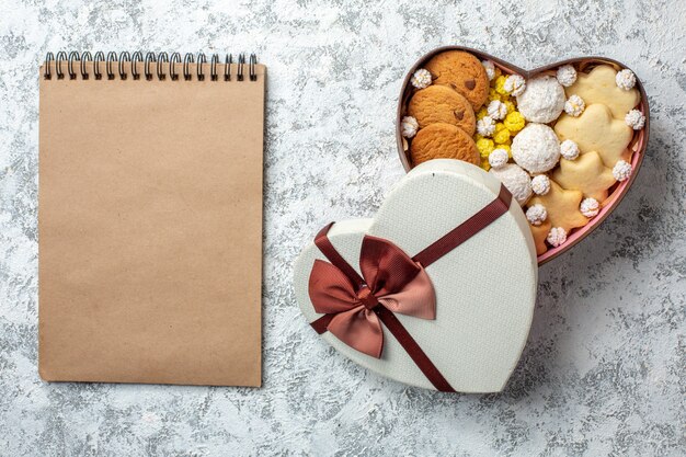 Vista dall'alto deliziosi dolci biscotti biscotti e caramelle all'interno di una scatola a forma di cuore su una superficie bianca torta di zucchero dolce yummy