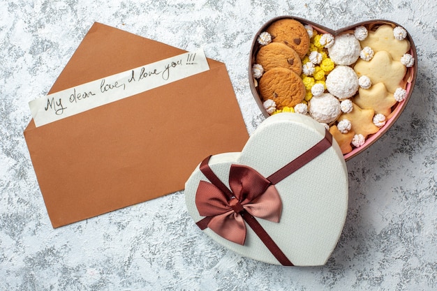 Vista dall'alto deliziosi dolci biscotti biscotti e caramelle all'interno di una scatola a forma di cuore su una superficie bianca torta di zucchero tè dolce yummy cake