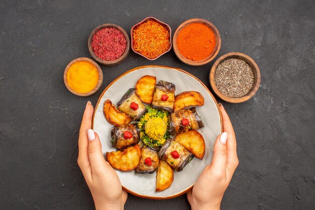 Vista dall'alto deliziosi involtini di melanzane piatto cotto con patate al forno e condimenti su sfondo scuro piatto cena cibo cucina pasto patate