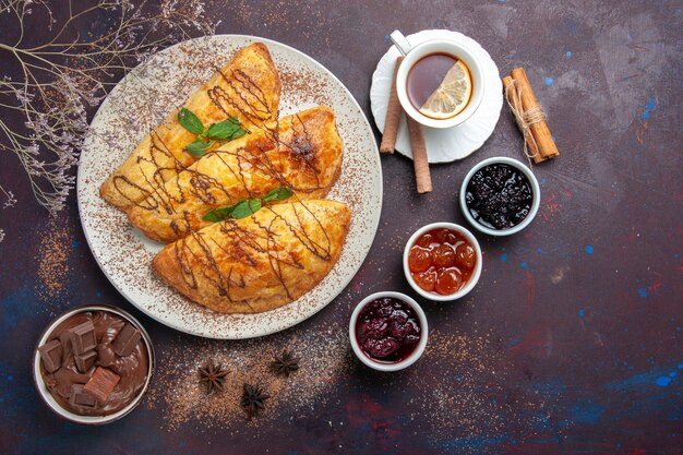 Vista dall'alto deliziosi pasticcini al forno con tazza di tè e marmellata su spazio viola scuro