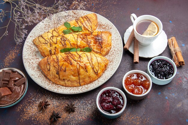 Vista dall'alto deliziosi pasticcini al forno con una tazza di marmellata di tè su uno spazio buio