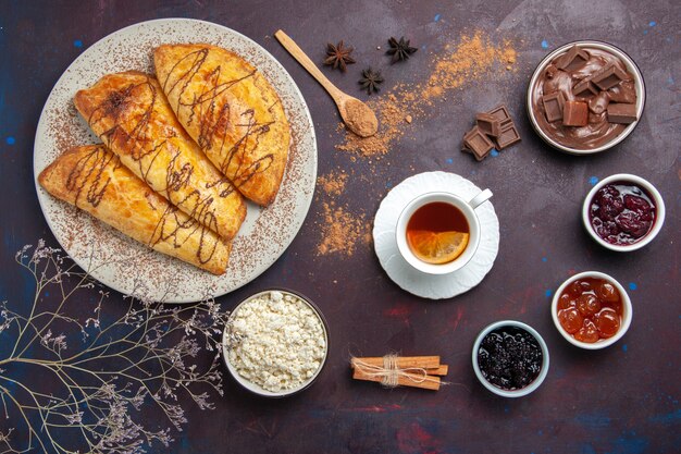 Vista dall'alto deliziosi pasticcini al forno con una tazza di marmellata di tè su uno spazio buio