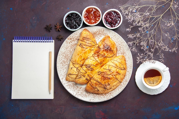 Vista dall'alto deliziosi pasticcini al forno con una tazza di marmellata di tè su uno spazio buio