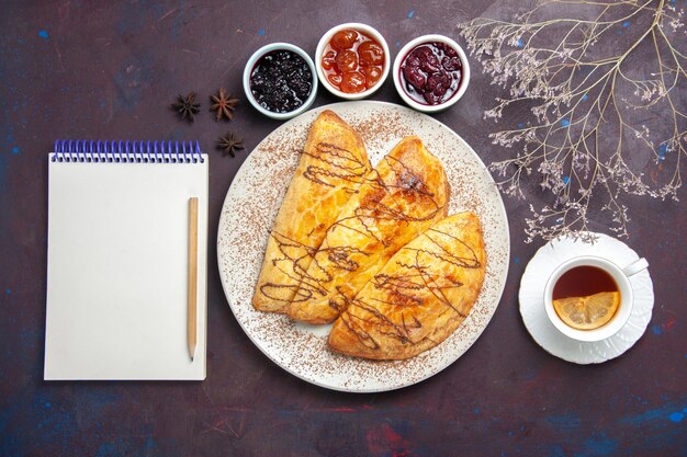 Vista dall'alto deliziosi pasticcini al forno con una tazza di marmellata di tè su uno spazio buio