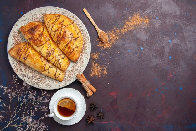 Vista dall'alto deliziosi pasticcini al forno con una tazza di tè nello spazio buio