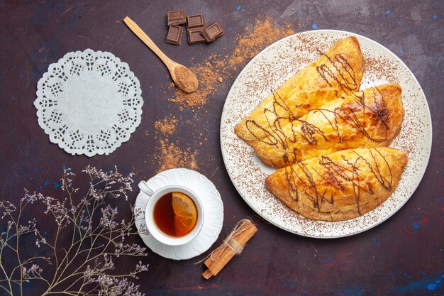 Vista dall'alto deliziosi pasticcini al forno con una tazza di tè nello spazio buio