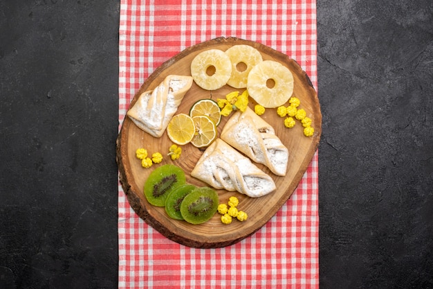 Vista dall'alto deliziosi pasticcini con anelli di ananas essiccati e kiwi su uno spazio grigio scuro