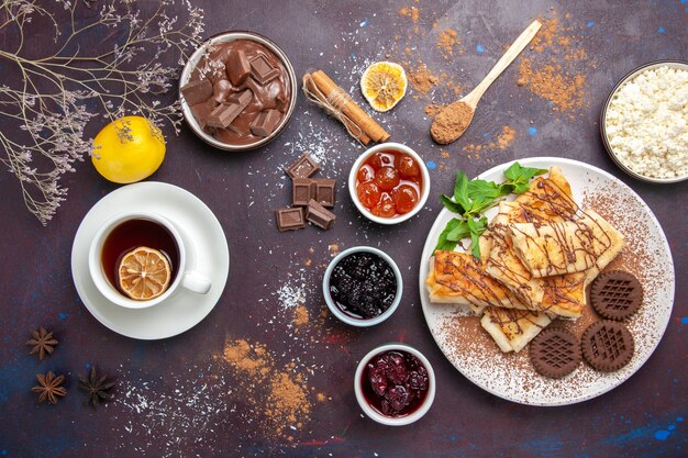 Vista dall'alto deliziosi pasticcini dolci con biscotti e tazza di tè in uno spazio buio