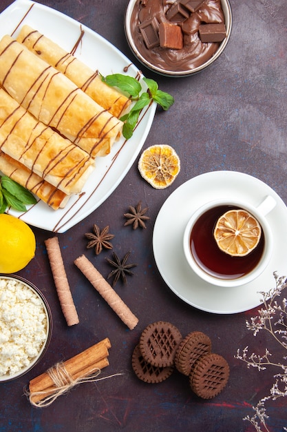 Vista dall'alto deliziosi pasticcini dolci con biscotti e tè nello spazio buio