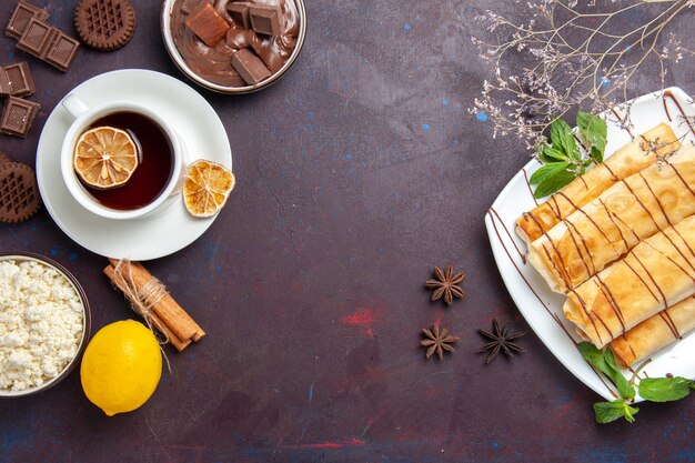 Vista dall'alto deliziosi pasticcini dolci con una tazza di tè al cioccolato e biscotti nello spazio buio