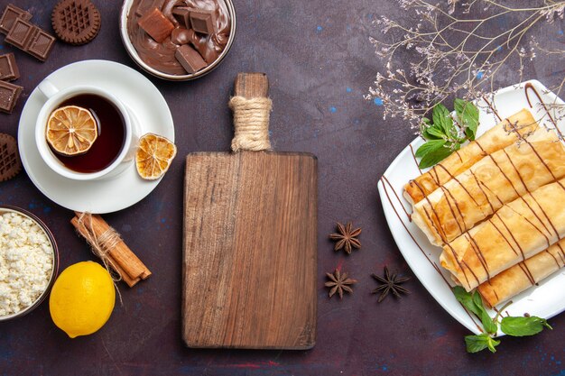 Vista dall'alto deliziosi pasticcini dolci con una tazza di tè al cioccolato e biscotti sulla scrivania scura