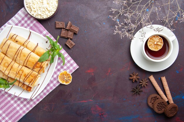 Vista dall'alto deliziosi pasticcini dolci con una tazza di tè nello spazio buio