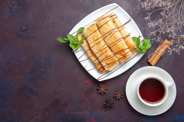 Vista dall'alto deliziosi pasticcini dolci con una tazza di tè nello spazio buio