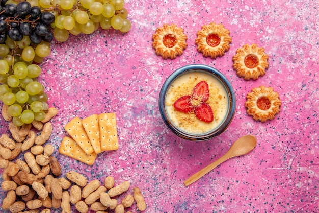 Vista dall'alto delizioso dessert cremoso con uva fresca biscotti cracker e arachidi sulla superficie rosa chiaro dessert gelato frutti di bosco crema dolce