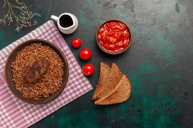 Vista dall'alto delizioso grano saraceno cotto con cotoletta e pane scuro sul piatto di verdure cibo pasto ingrediente superficie verde scuro