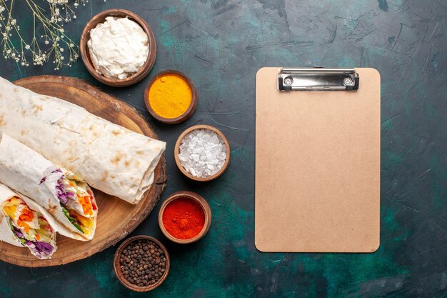 Vista dall'alto delizioso panino di carne fatto di carne alla griglia allo spiedo con condimenti e blocco note sulla scrivania blu panino hamburger carne pasto pranzo cibo