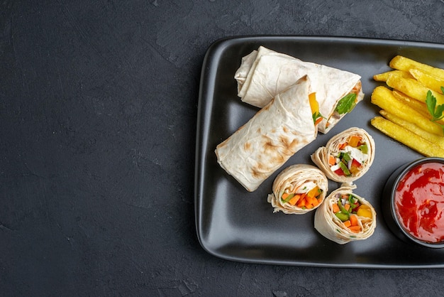 Vista dall'alto delizioso panino pita affettato shawarma con patatine fritte e ketchup su superficie scura