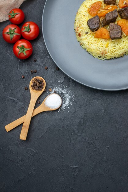 Vista dall'alto delizioso riso cotto pilaf con fette di carne e pomodori sulla superficie scura