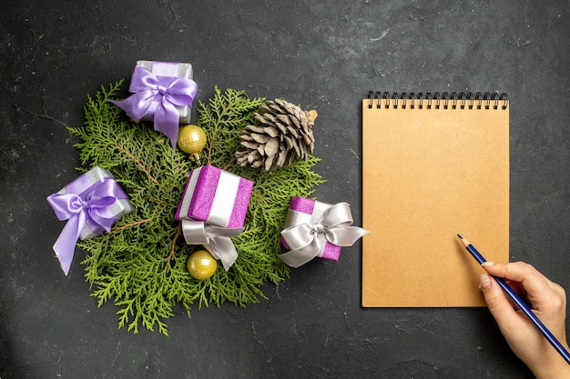 Vista dall'alto dell'accessorio colorato per la decorazione dei regali di capodanno e del cono di conifere accanto al notebook su sfondo scuro