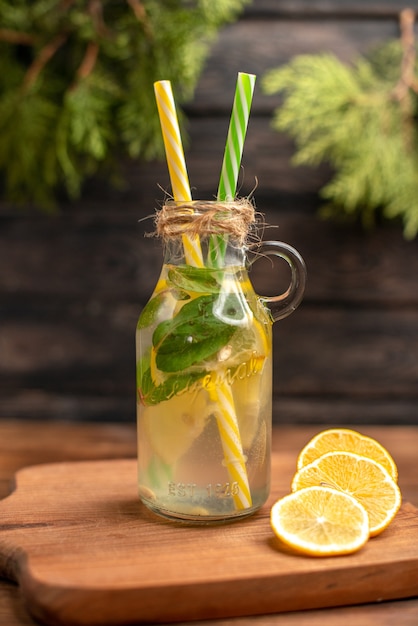 Vista dall'alto dell'acqua disintossicante fresca in un bicchiere servito con tubi e lime al limone su un tagliere di legno