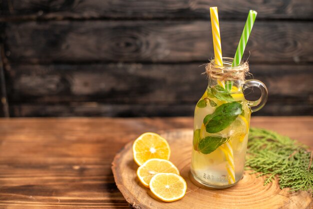 Vista dall'alto dell'acqua disintossicante fresca in un bicchiere servito con tubi e lime al limone sul lato sinistro su un vassoio marrone
