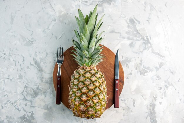 Vista dall'alto dell'intero ananas dorato fresco sul coltello a forchetta del tagliere sulla superficie di marmo