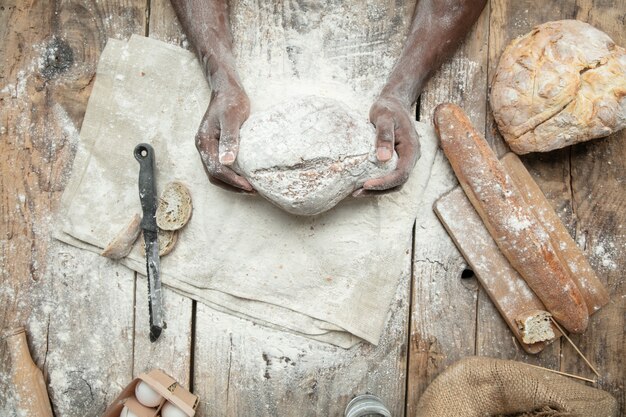 Vista dall'alto dell'uomo afro-americano cuochi cereali freschi, pane, crusca sulla tavola di legno. Mangiare gustoso, nutrizione, prodotto artigianale