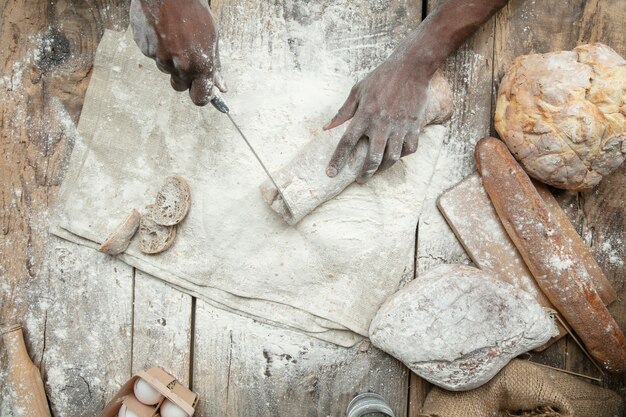 Vista dall'alto dell'uomo afro-americano cuochi cereali freschi, pane, crusca sulla tavola di legno. Mangiare gustoso, nutrizione, prodotto artigianale